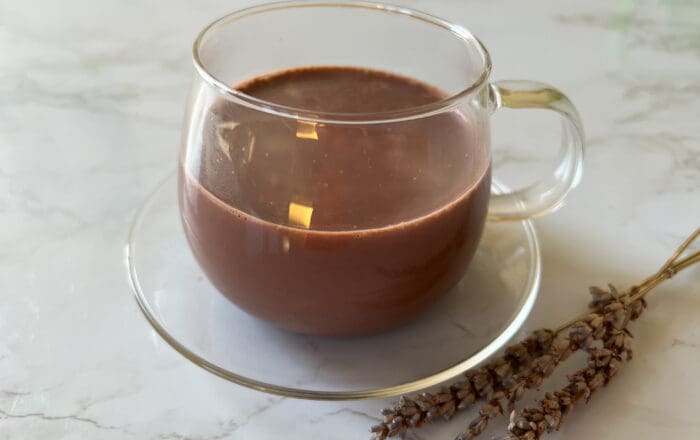 Hot chocolate served in a glass cup and saucer displayed on a marble table top with sprigs of dried lavender next to it