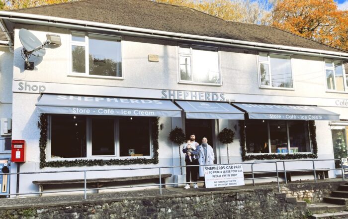 A white painted shop with a sign reading Shepherds, with a man and woman standing outside the door