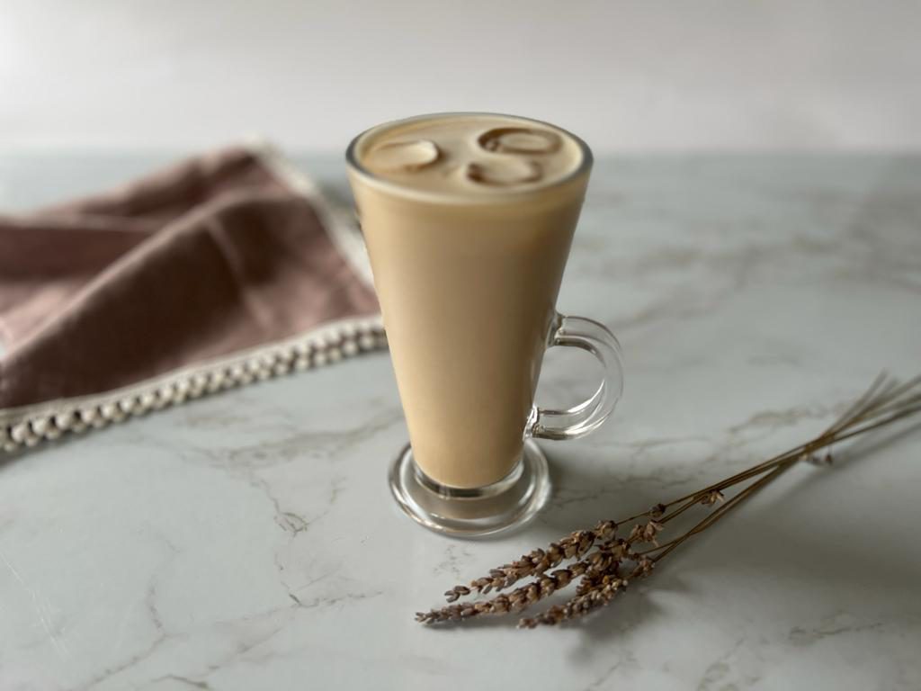An iced latte displayed on a marble table top, with a coffee-coloured napkin and some dried lavender