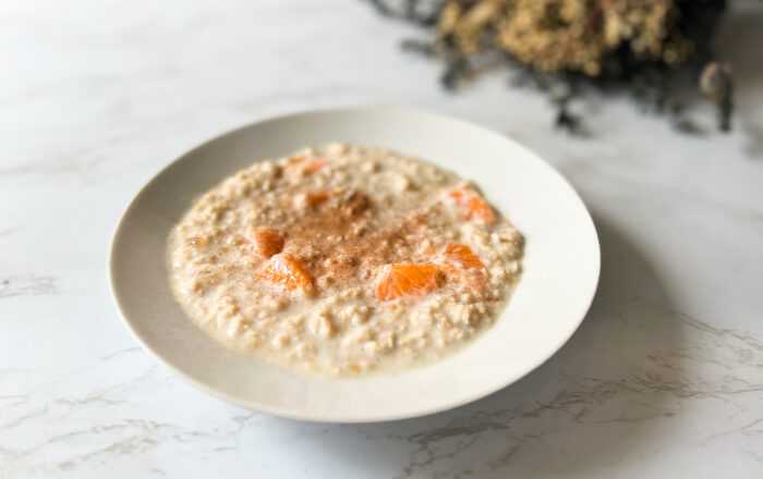 Porridge topped with cinnamon and orange segments, displayed in a white bowl on a marble table top