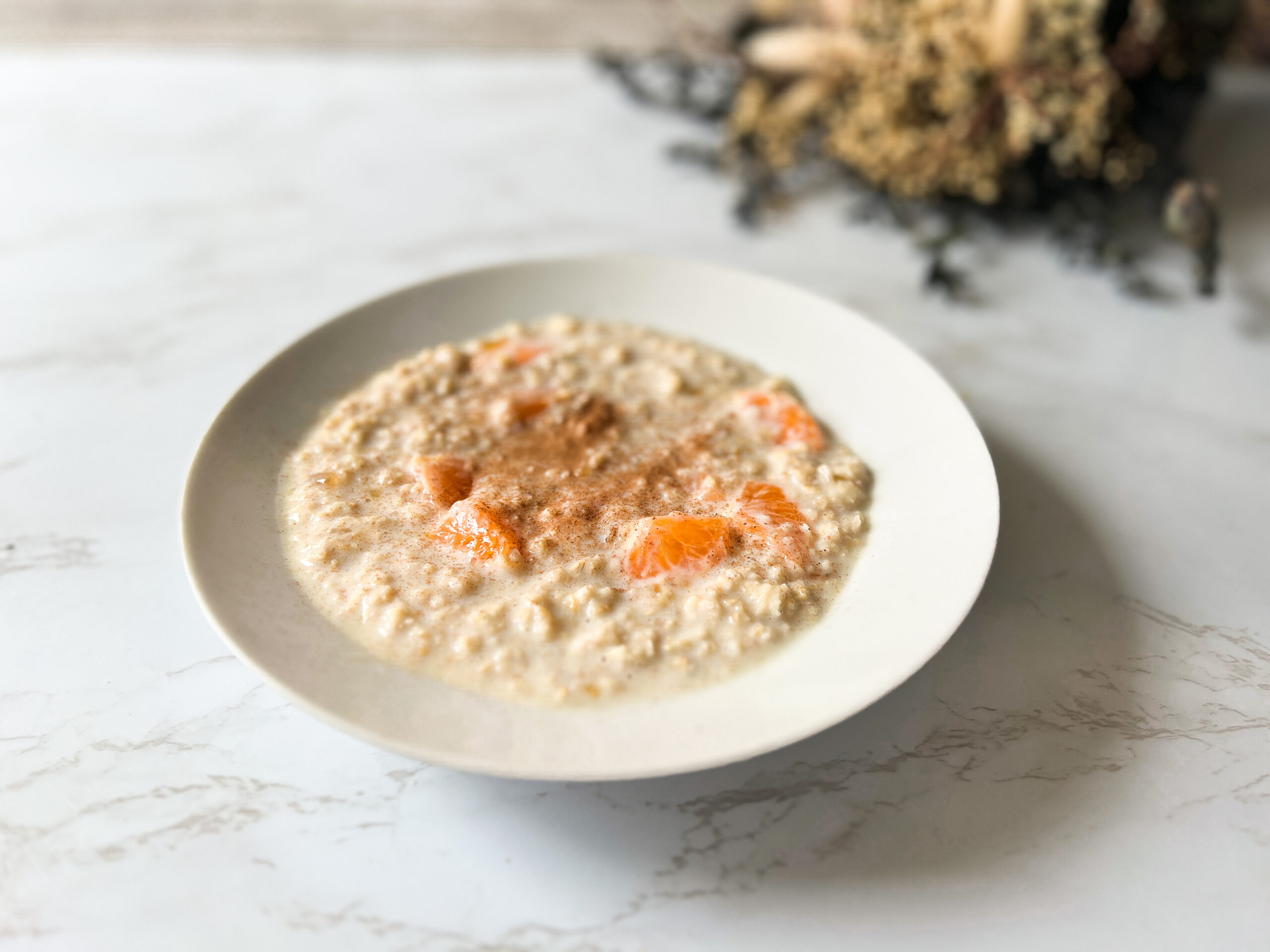 Porridge topped with cinnamon and orange segments, displayed in a white bowl on a marble table top